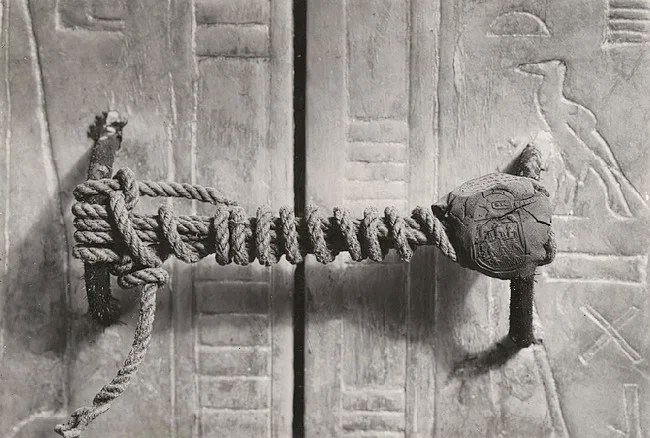 Gros plan en noir et blanc du grand naos (chapelle funéraire) en bois doré de Toutankhamon, montrant ses portes scellées encore fermées avec la corde et le sceau d'argile intacts, dans la chambre funéraire de la tombe KV62 à Louxor, photographie de Harry Burton, 1923.