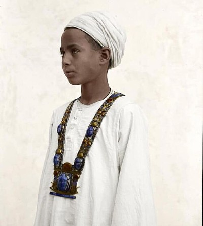 Photographie en noir et blanc de Harry Burton représentant un jeune garçon égyptien, Hussein Abdel Rassul, portant un collier pectoral en or et lapis-lazuli provenant du tombeau de Toutankhamon, Vallée des Rois à Louxor, vers 1923.
