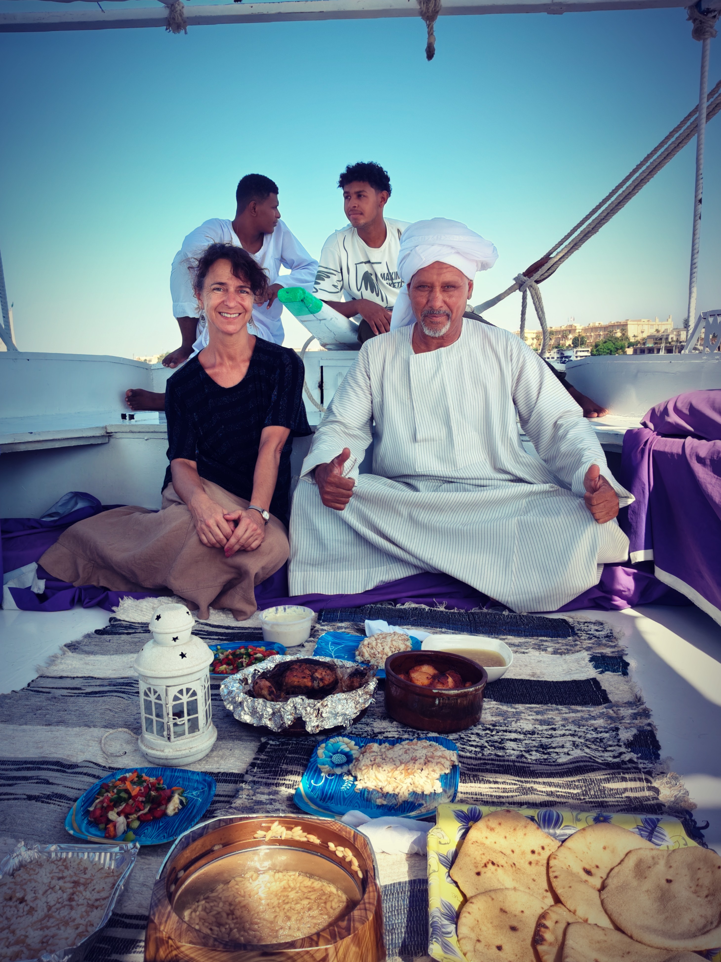 voyageuse solo en Egypte à Louxor appréciant le dîner traditionnel égyptien à bord posant avec le capitaine de felouque et son équipage.