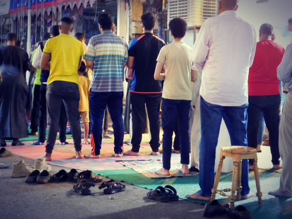 Hommes et enfants priant avec recueillement lors d'une prière de Tarawih en plein air, sous la lumière des lampadaires, illustrant la dévotion du mois de Ramadan en Egypte