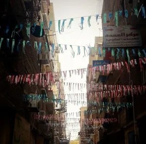 Rue commerçante égyptienne décorée pour le Ramadan avec une arche de fanions  colorés traversant la chaussée, créant une ambiance festive.