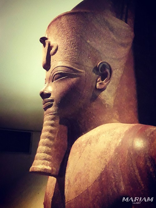 Statue en granit rouge d'Amenhotep III au Musée de Louxor, représentant le pharaon de manière idéalisée selon les canons traditionnels de l'art égyptien.