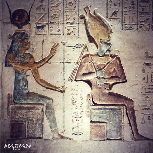 Relief ptolémaïque de la chapelle sud du temple d'Hathor à Deir el-Médineh représentant Isis, coiffée des cornes hathoriques et du disque solaire, levant les mains en signe de protection au-dessus d'Osiris assis sur son trône