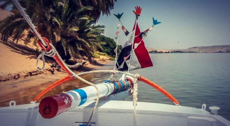 Felouque amarrée sur une rive sauvage du Nil.  L'embarcation traditionnelle à voile est immobilisée sur une berge déserte, loin de tout. Aucun autre bateau en vue. Paysage désertique et eau calme. croisière sur le Nil en felouque 4 nuits au départ d'Assouan