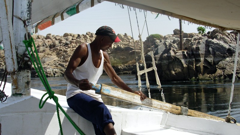 Felouquier ajustant la voile sur une felouque traditionnelle du Nil à Assouan, balade au coucher du soleil