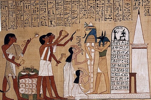 Vignette du Livre des Morts de Hounéfer représentant le rituel de l'ouverture de la bouche, avec la momie du défunt soutenue par Anubis, ses proches en deuil, des prêtres officiant, un tombeau blanc avec petite pyramide, et une table d'instruments rituels.