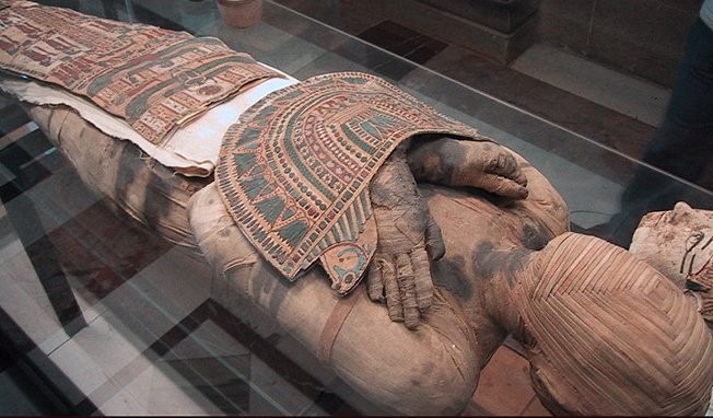Photographie de la momie "Bashiri" surnommée "l'Intouchable", exposée au Musée Égyptien du Caire, présentant ses bandelettes de lin disposées en un motif géométrique complexe évoquant la base des pyramides de Gizeh.