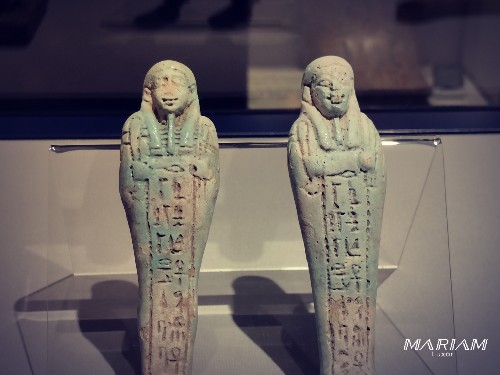 Photographie de plusieurs statuettes funéraires oushebtis en faïence égyptienne de couleur bleue et verte, exposées dans une vitrine du Musée de la Momification de Louxor.